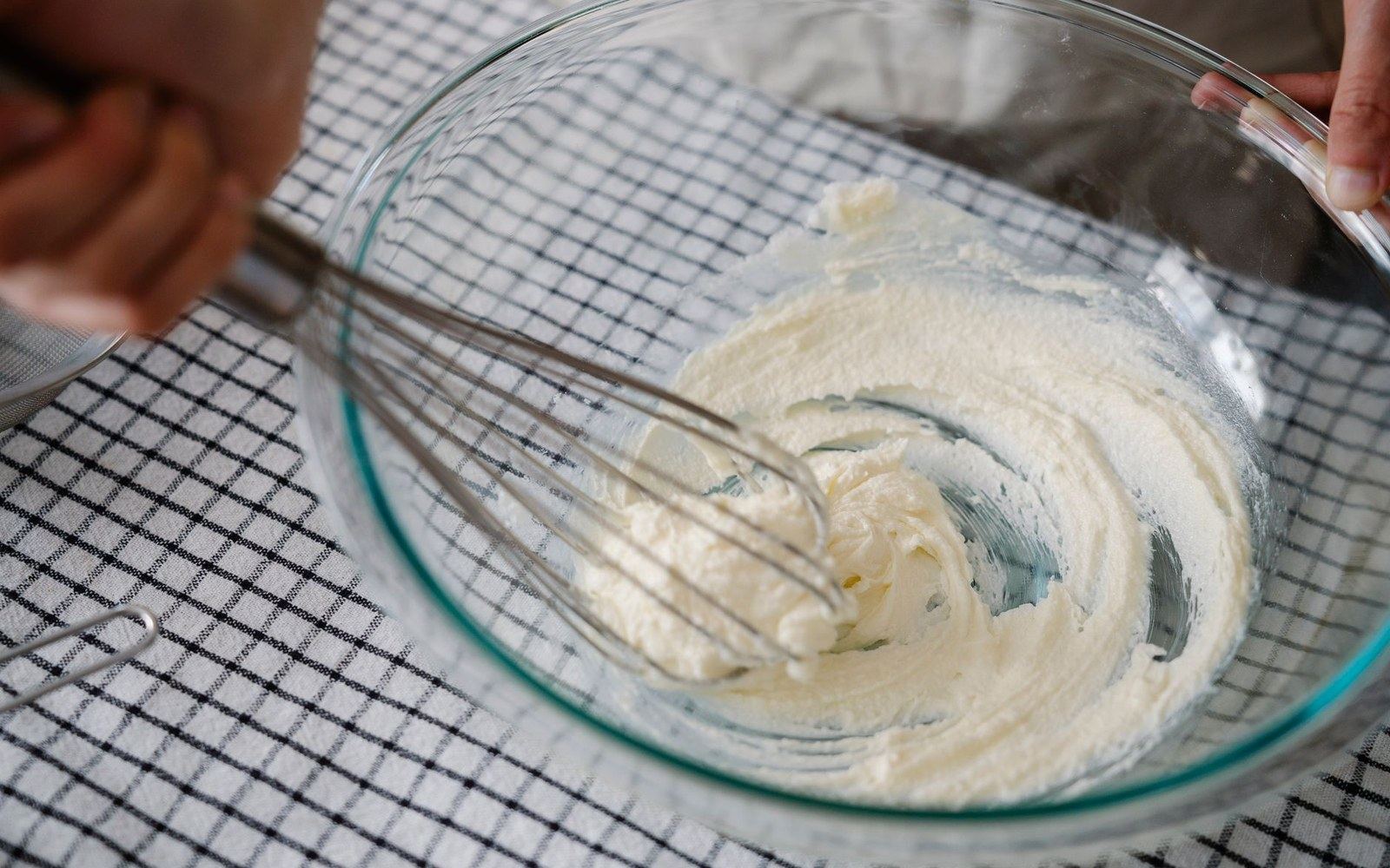 Whisking whipped cream in a glass bowl on a checkered towel