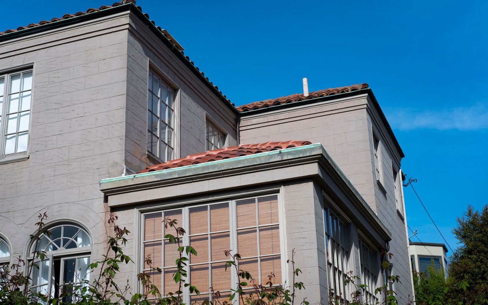 Stucco building exterior with terracotta tile roof and paned windows against a blue sky