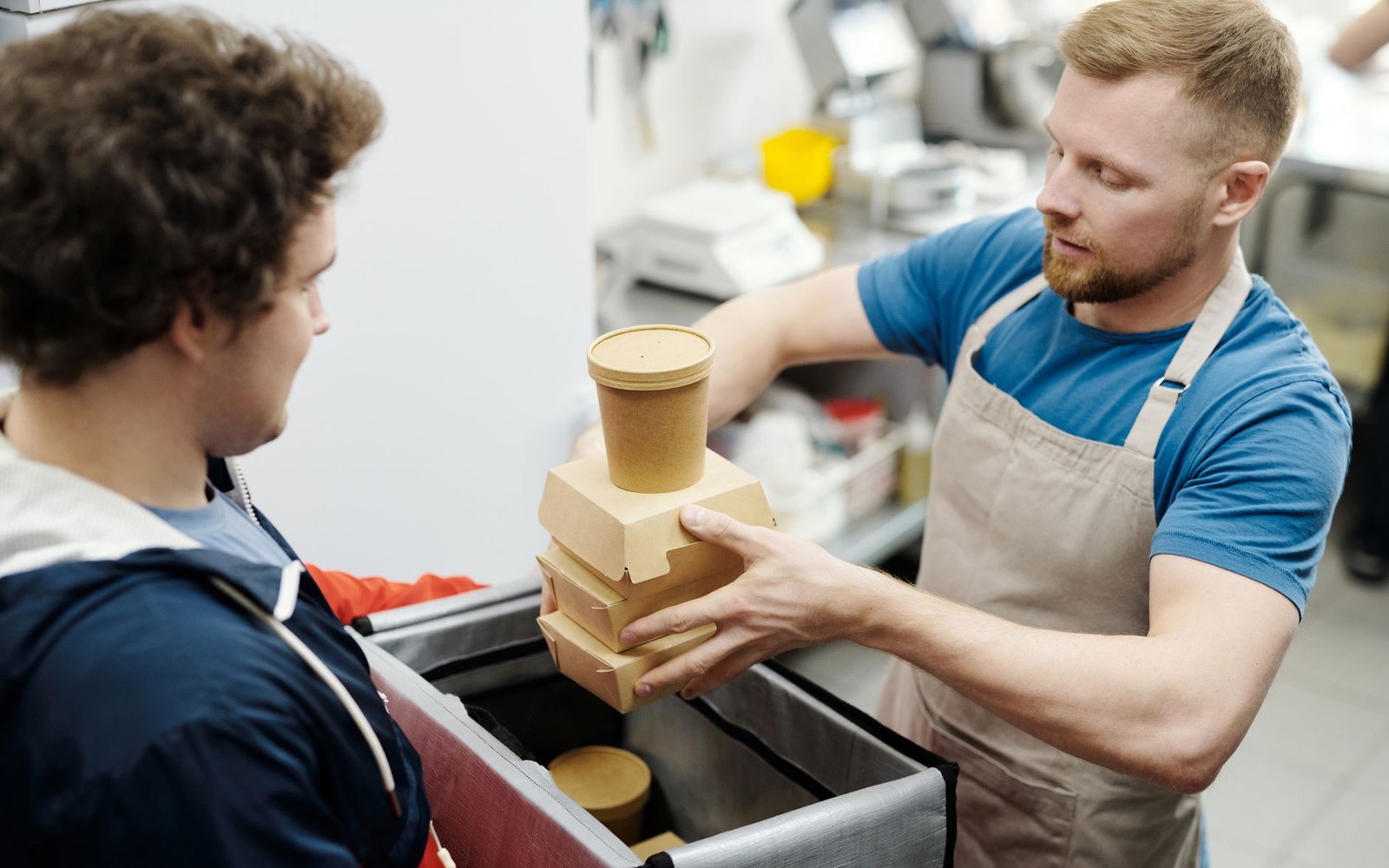 An apron-clad worker hands stacked takeout containers to a customer at a counter