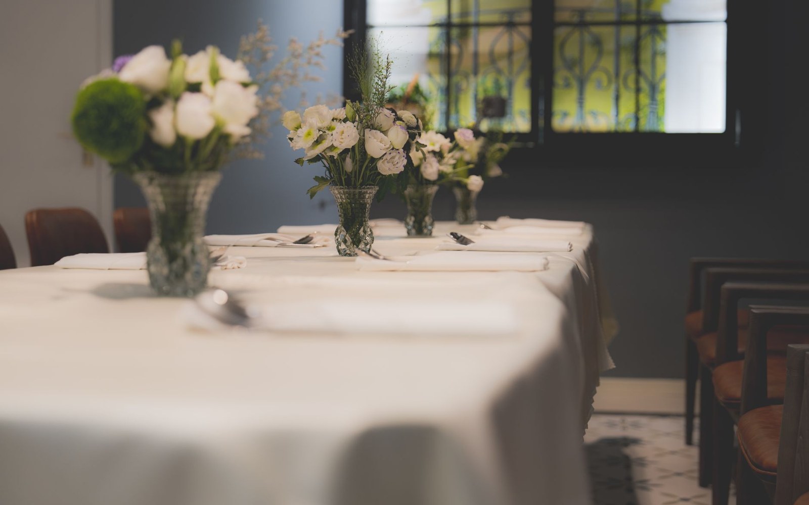 White floral centerpieces line a long dining table set with cloth napkins and cutlery