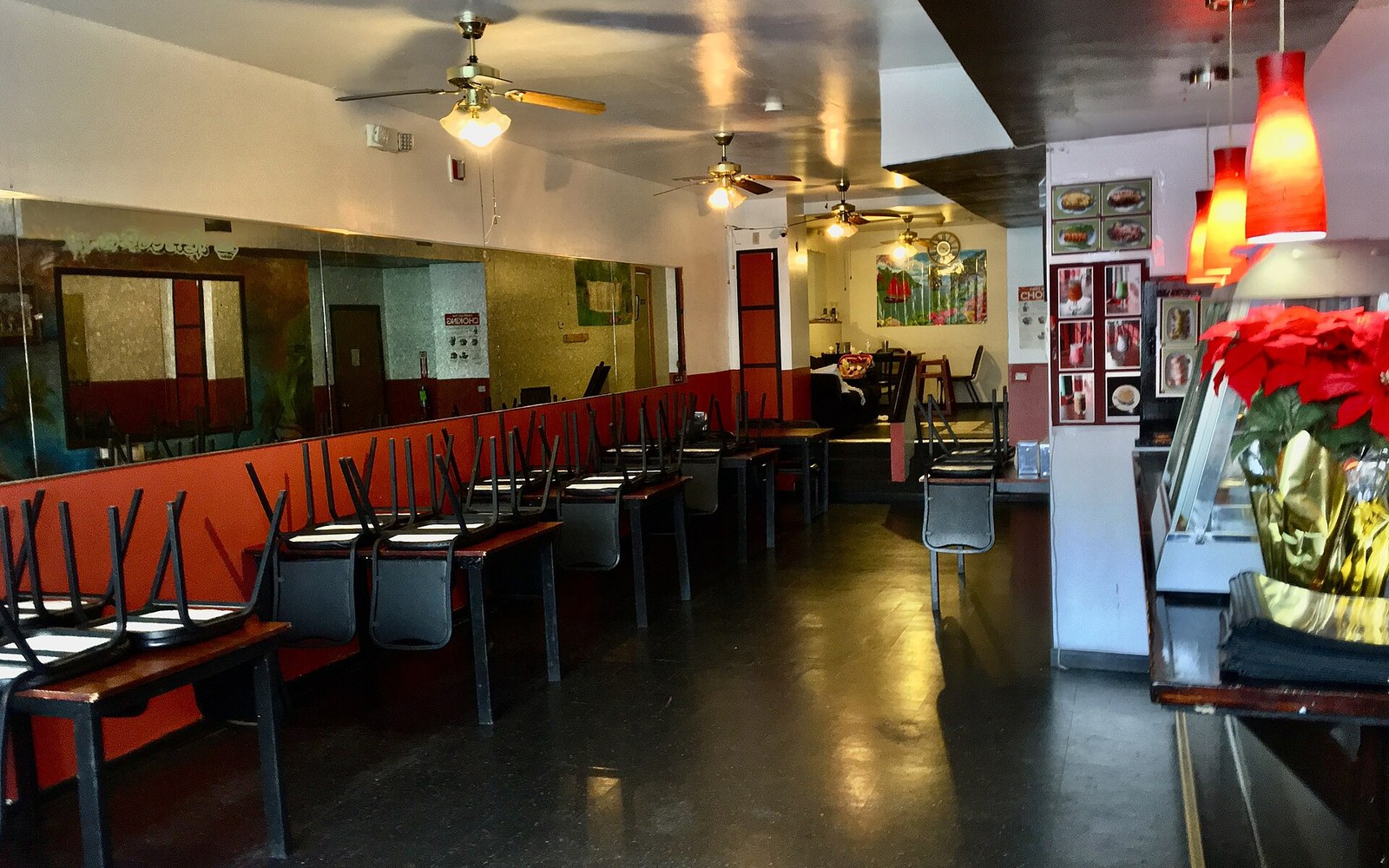 Empty restaurant dining room with chairs stacked on tables and red pendant lights