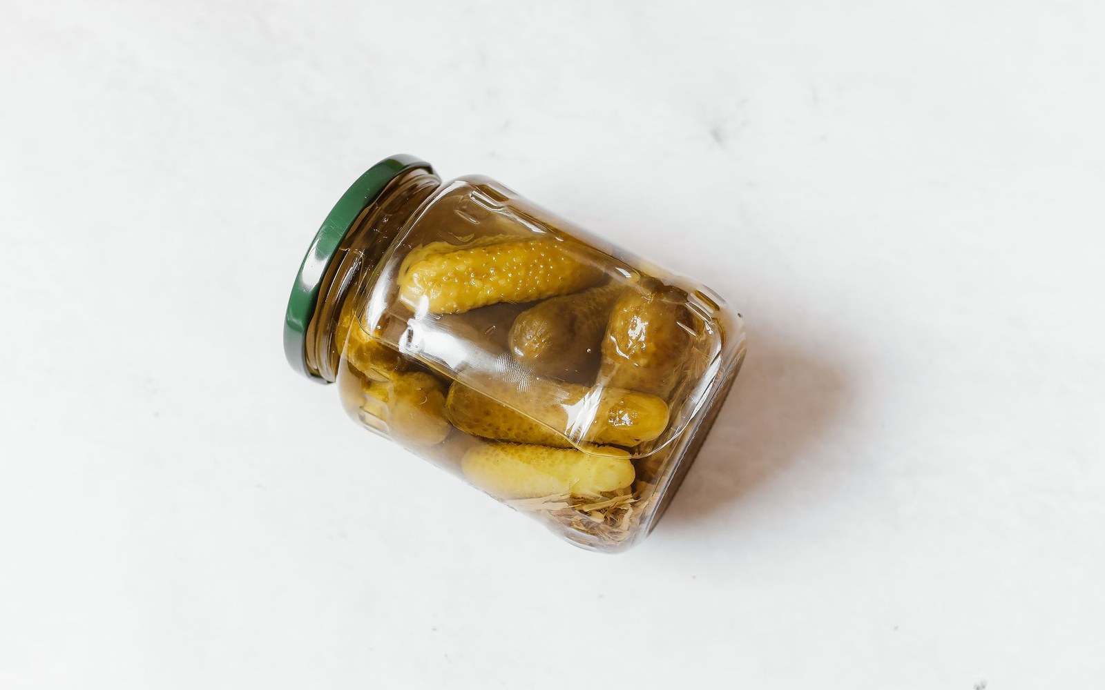 Whole pickled cucumbers packed inside a glass jar with a green lid