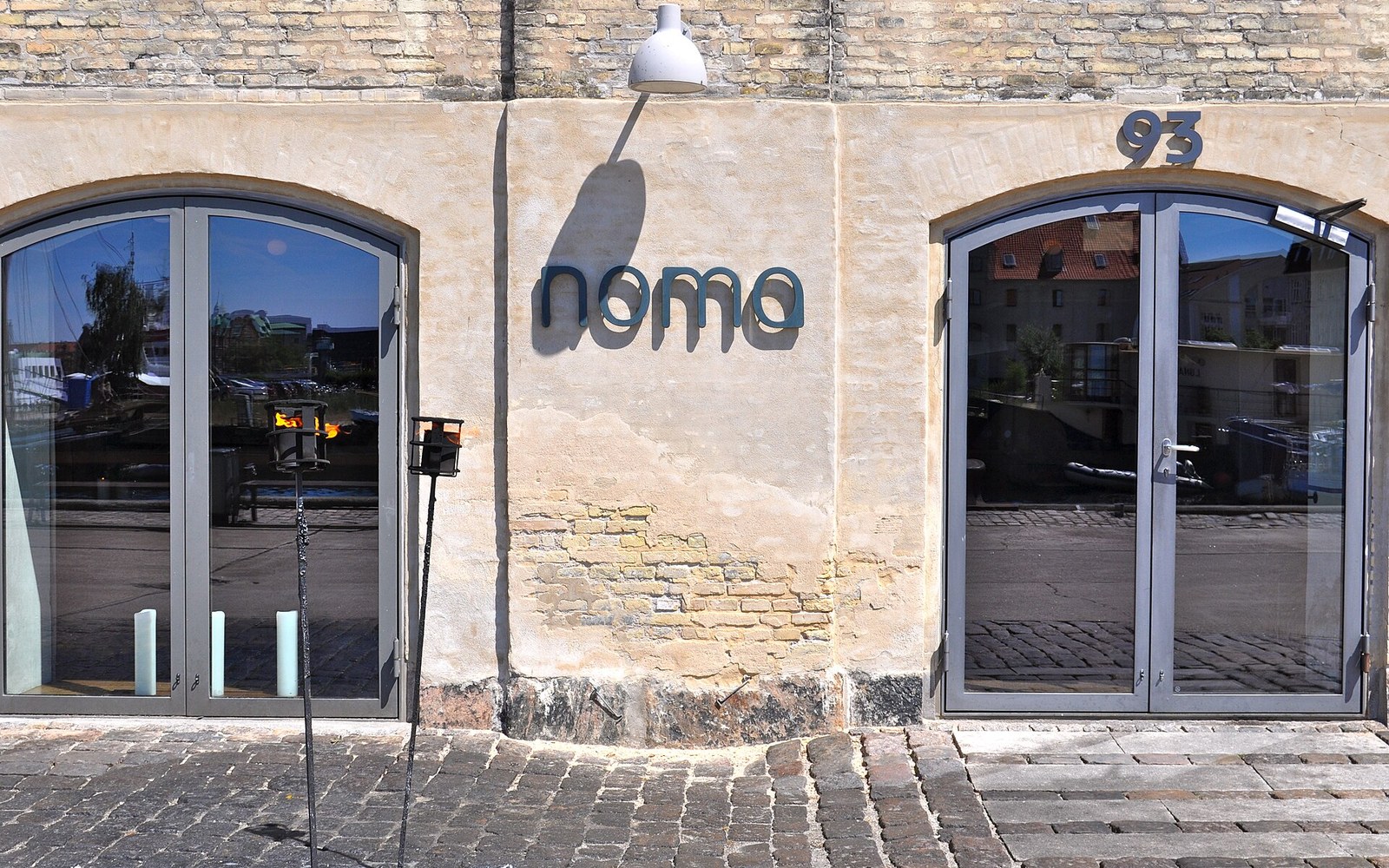 Noma restaurant entrance with arched glass doors and lettered sign on brick wall