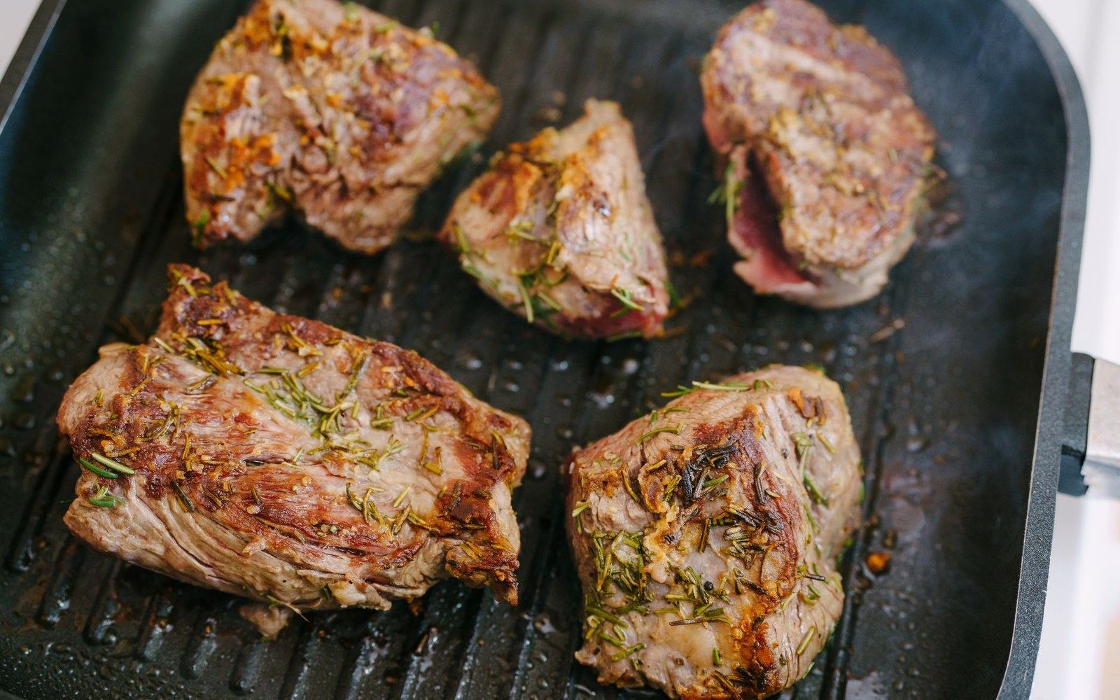 Rosemary-crusted lamb shoulder pieces searing on a ridged grill pan