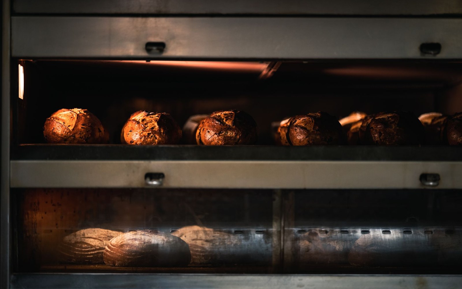 Rows of freshly baked sourdough loaves cooling on shelves inside a commercial oven