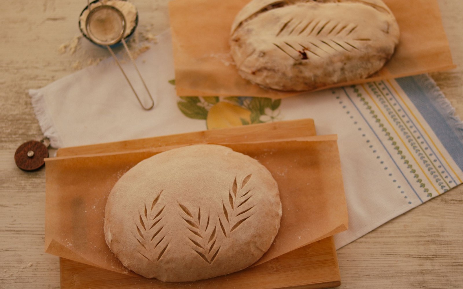 Two round sourdough loaves scored with wheat-stalk patterns before baking, dusted with flour
