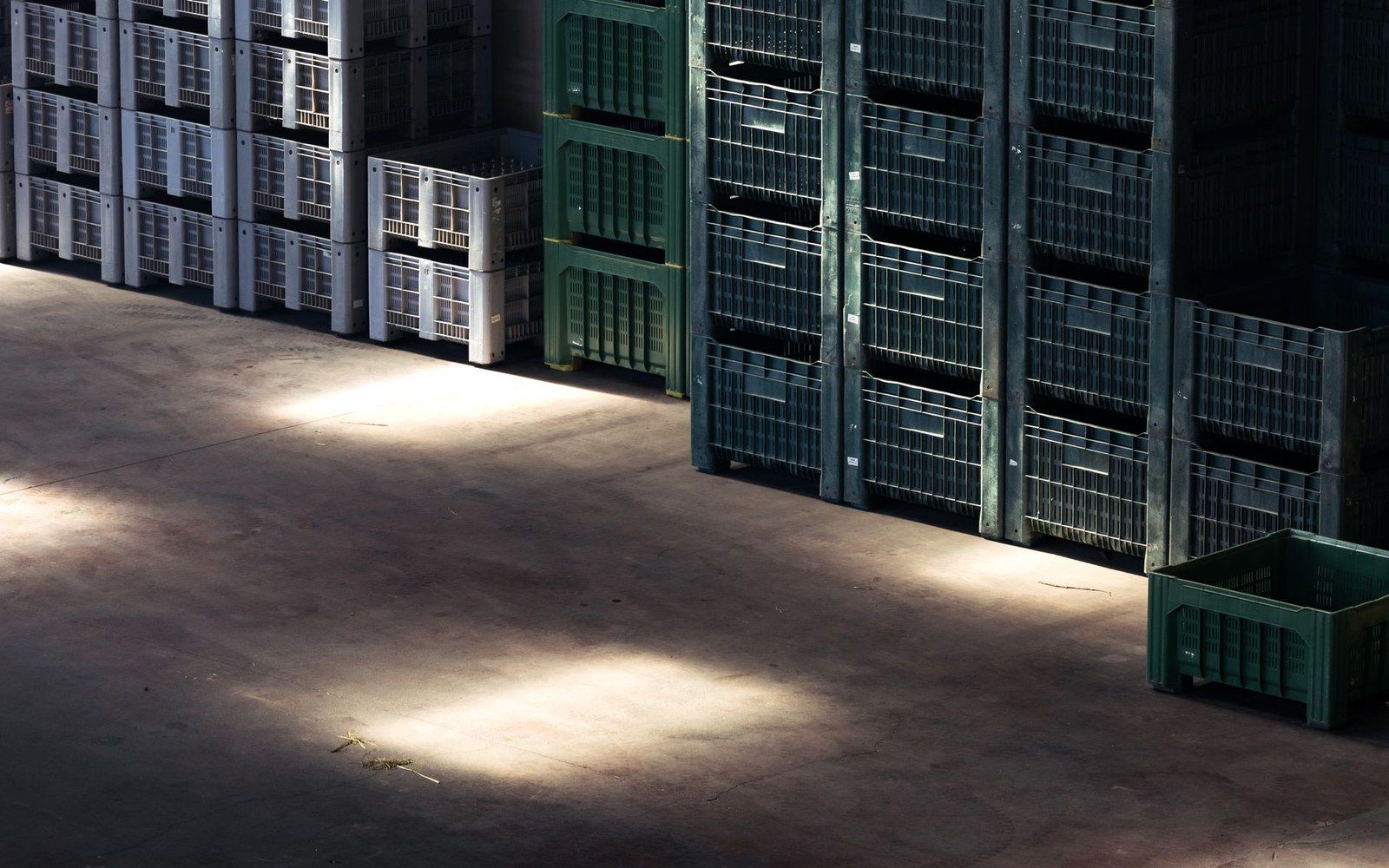 Stacked plastic crates in white and green form tall columns inside a warehouse