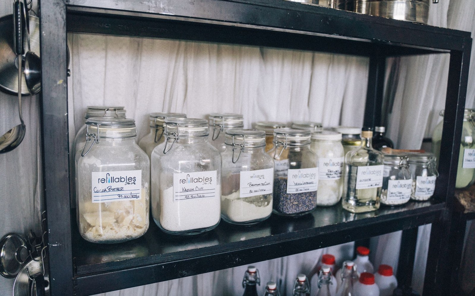 A cold-room shelf holding labelled containers, a hanging carcass partially visible at the left edge, adult kitchen worker in whites checking a label